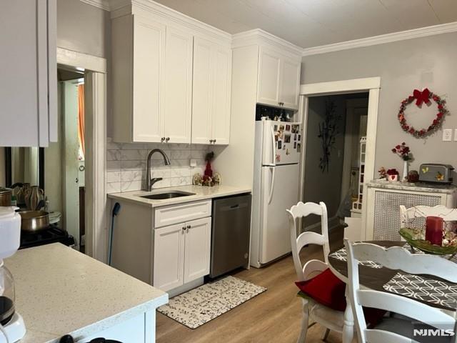 kitchen featuring a sink, light wood-style floors, light countertops, stainless steel dishwasher, and freestanding refrigerator