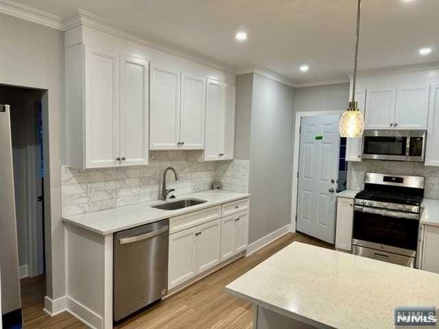 kitchen with recessed lighting, stainless steel appliances, light countertops, a sink, and crown molding