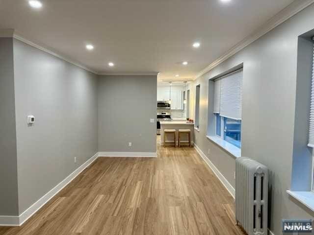 unfurnished living room with recessed lighting, radiator heating unit, ornamental molding, light wood finished floors, and baseboards