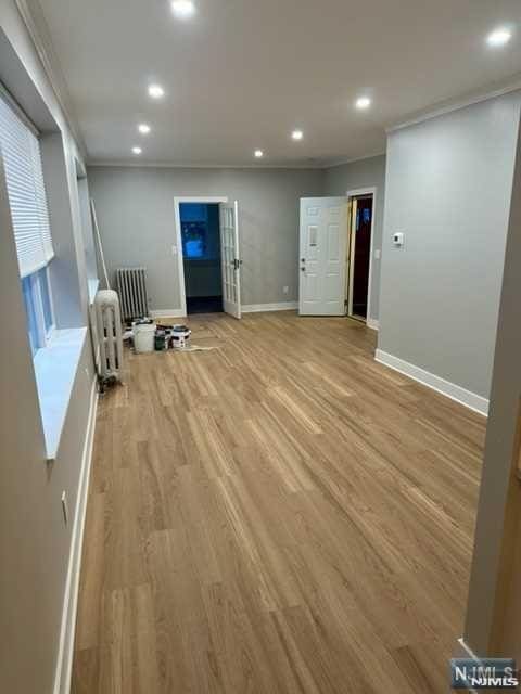 interior space with recessed lighting, crown molding, radiator heating unit, light wood-style flooring, and baseboards