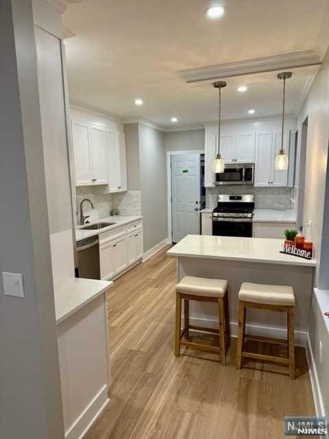 kitchen featuring a sink, tasteful backsplash, crown molding, white cabinetry, and appliances with stainless steel finishes