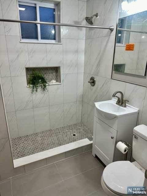bathroom with tile patterned floors, a shower stall, tile walls, toilet, and vanity