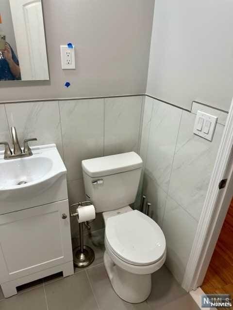 half bathroom with vanity, toilet, tile patterned flooring, and tile walls