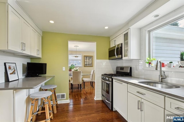 kitchen featuring appliances with stainless steel finishes, a sink, glass insert cabinets, and white cabinets