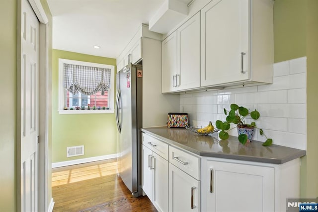 kitchen with dark countertops, wood finished floors, freestanding refrigerator, and white cabinetry