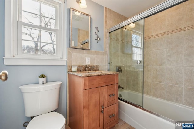 bathroom featuring shower / bath combination with glass door, vanity, toilet, and tile walls