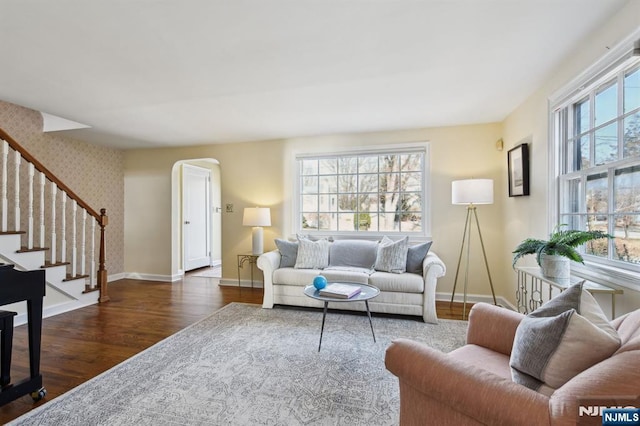 living room featuring dark wood-type flooring, a healthy amount of sunlight, stairway, and wallpapered walls