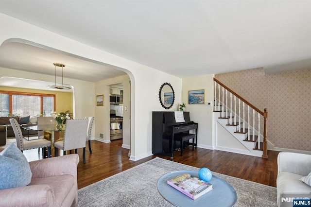 living area featuring dark wood-style floors, stairway, arched walkways, and wallpapered walls