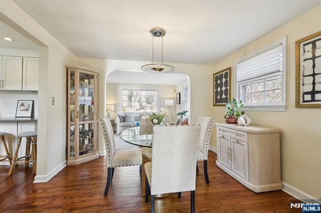 dining area with dark wood-style floors, baseboards, and arched walkways