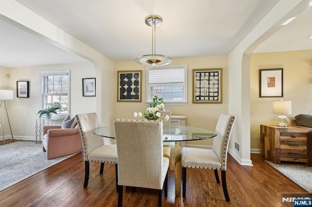 dining area featuring arched walkways, dark wood-style flooring, visible vents, and baseboards