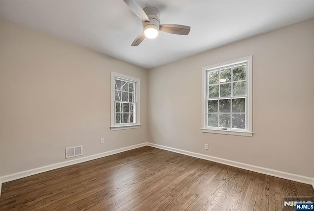 empty room with baseboards, visible vents, dark wood finished floors, and a ceiling fan