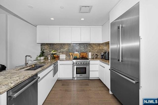 kitchen featuring white cabinetry, light stone countertops, sink, tasteful backsplash, and high quality appliances