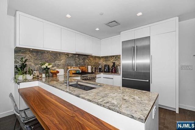 kitchen with light stone countertops, built in fridge, sink, white cabinetry, and kitchen peninsula