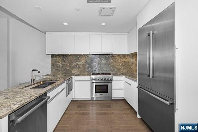 kitchen featuring sink, backsplash, light stone counters, premium appliances, and white cabinets