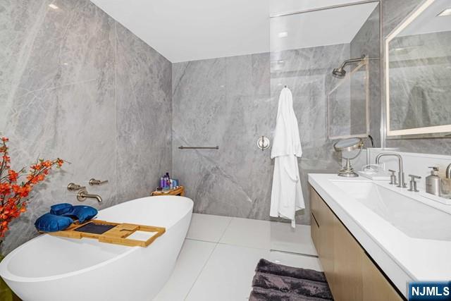 bathroom featuring independent shower and bath, tile patterned flooring, tile walls, and vanity