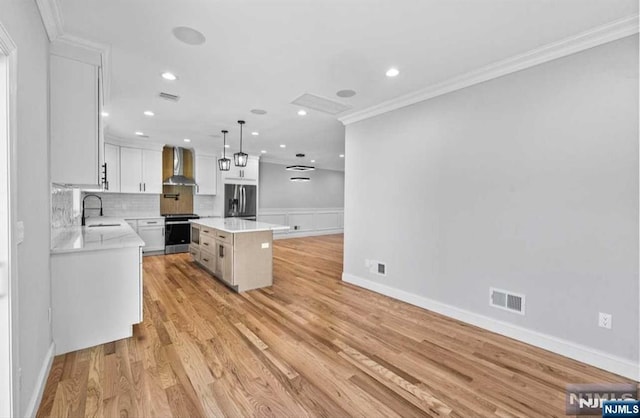 kitchen with stainless steel appliances, white cabinets, wall chimney range hood, pendant lighting, and a center island