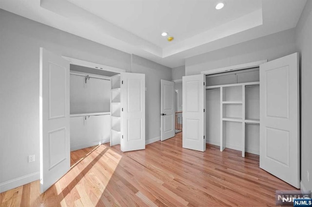 unfurnished bedroom featuring light hardwood / wood-style floors, a raised ceiling, and a closet