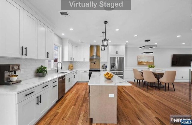 kitchen with appliances with stainless steel finishes, sink, a center island, wall chimney exhaust hood, and white cabinets