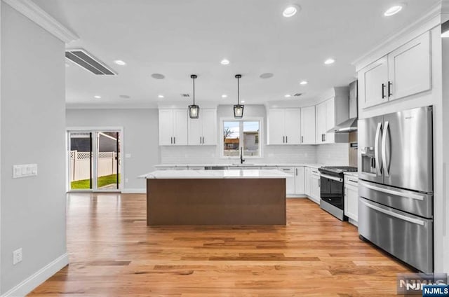 kitchen featuring a center island, decorative light fixtures, wall chimney range hood, stainless steel appliances, and white cabinets