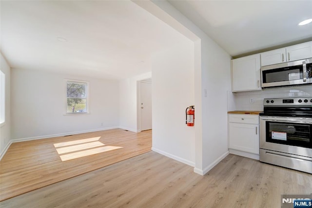 kitchen with appliances with stainless steel finishes, white cabinets, decorative backsplash, and light hardwood / wood-style flooring