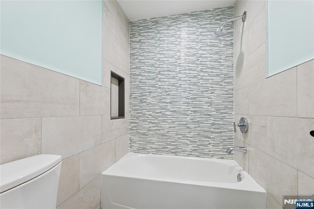 bathroom featuring washtub / shower combination, tile walls, and toilet