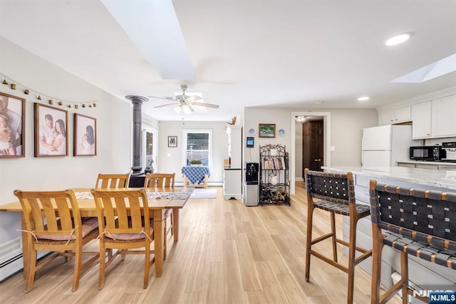 dining area with light wood-type flooring, a skylight, and ceiling fan