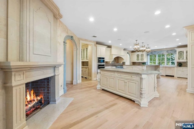 kitchen featuring hanging light fixtures, a high end fireplace, custom range hood, cream cabinets, and a kitchen island with sink