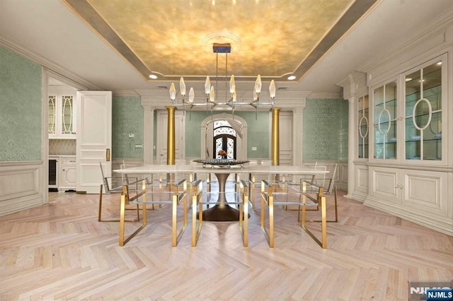 dining space with a raised ceiling, beverage cooler, ornamental molding, light parquet flooring, and decorative columns