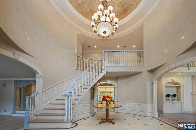 stairs with a tray ceiling, a towering ceiling, crown molding, and an inviting chandelier