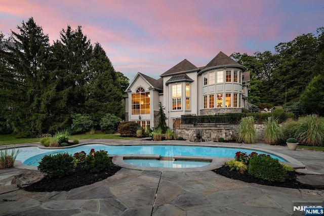 back house at dusk with a balcony, a patio area, and a pool with hot tub