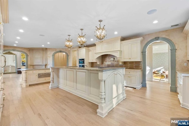 kitchen featuring an island with sink, pendant lighting, cream cabinetry, and light wood-type flooring