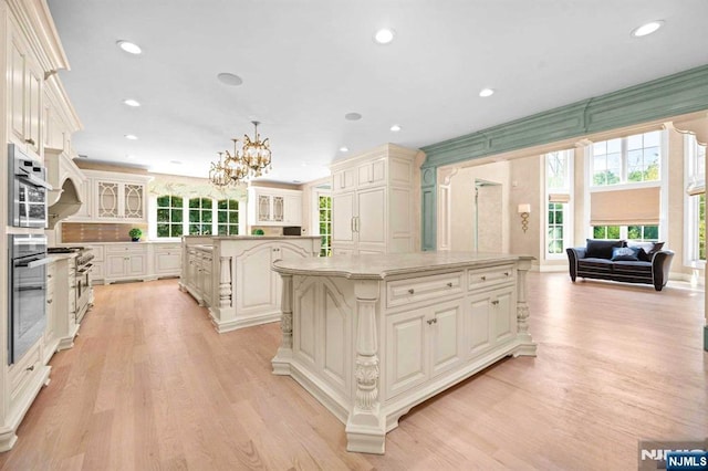 kitchen with a center island with sink, stainless steel appliances, decorative light fixtures, cream cabinetry, and light hardwood / wood-style floors