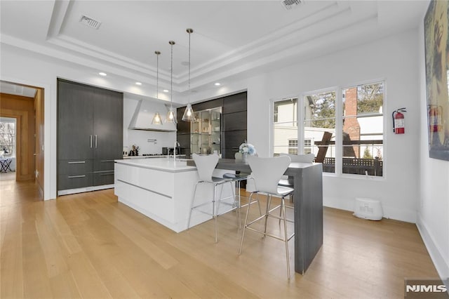 kitchen with modern cabinets, light countertops, decorative light fixtures, an island with sink, and a tray ceiling