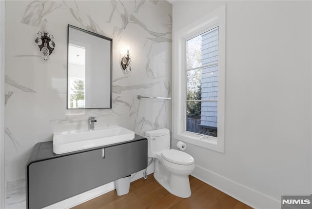 half bath with baseboards, vanity, toilet, and wood finished floors