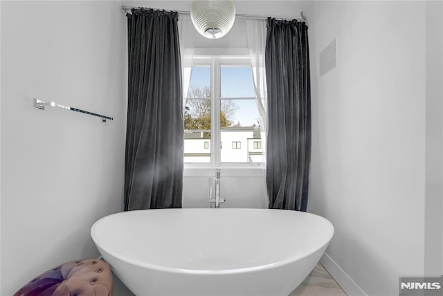 full bathroom with a freestanding tub, baseboards, and marble finish floor