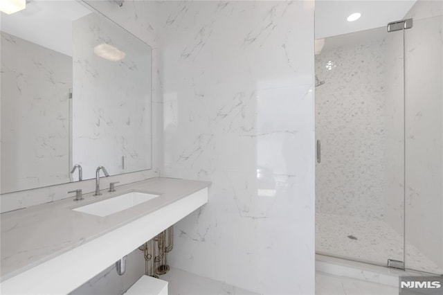 bathroom with a sink, recessed lighting, a marble finish shower, and stone wall