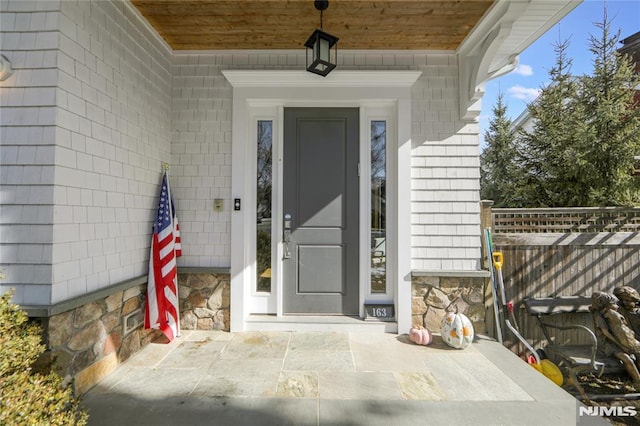 property entrance featuring stone siding and fence