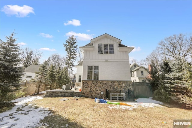 back of house with stone siding, fence, and board and batten siding