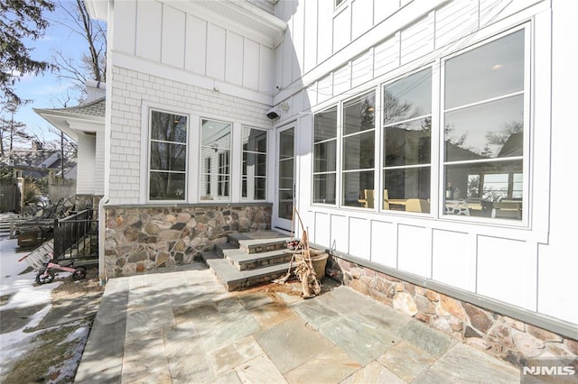 exterior space with entry steps, a patio, stone siding, fence, and board and batten siding