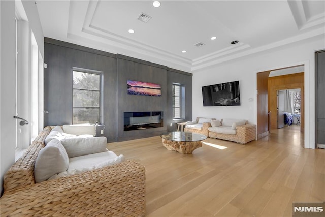 living room with a raised ceiling, visible vents, light wood finished floors, and a glass covered fireplace