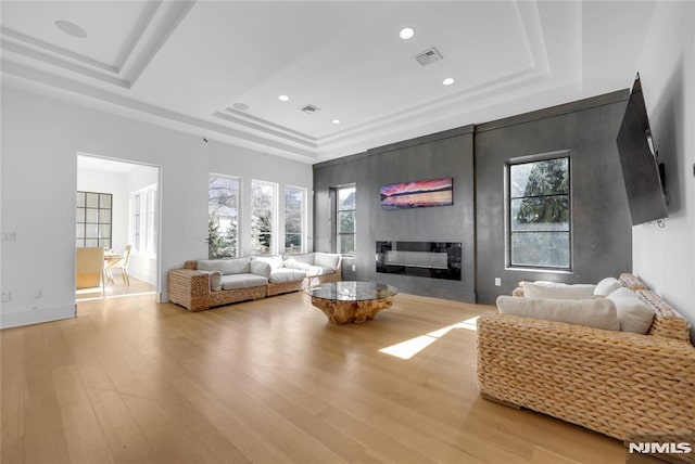 living room featuring visible vents, a raised ceiling, light wood-style floors, a wealth of natural light, and a large fireplace