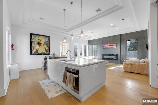 kitchen with a kitchen island with sink, visible vents, a tray ceiling, and open floor plan