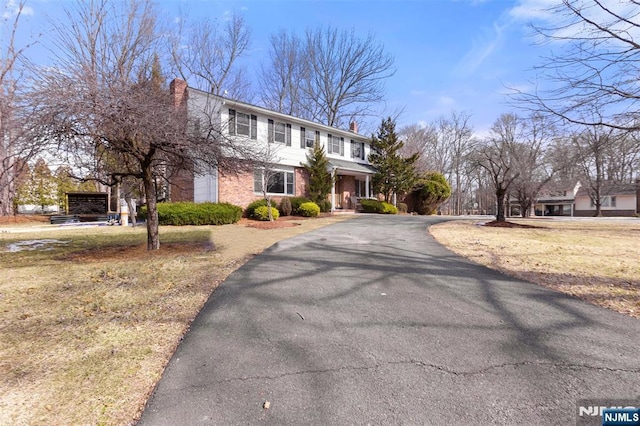 view of front facade featuring driveway, brick siding, and a chimney