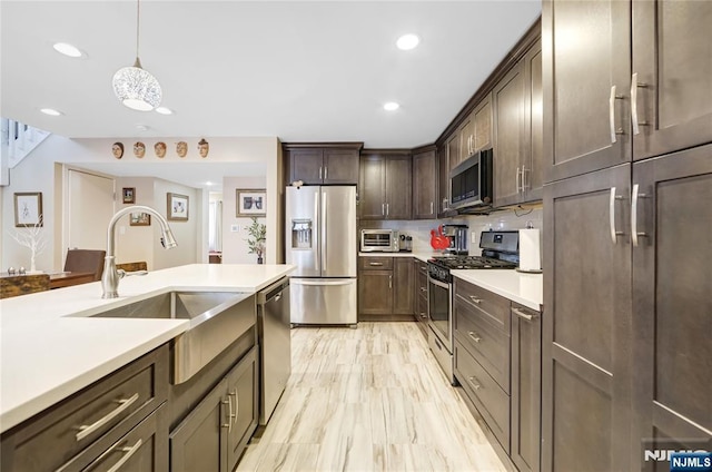 kitchen featuring dark brown cabinetry, tasteful backsplash, appliances with stainless steel finishes, light countertops, and a sink