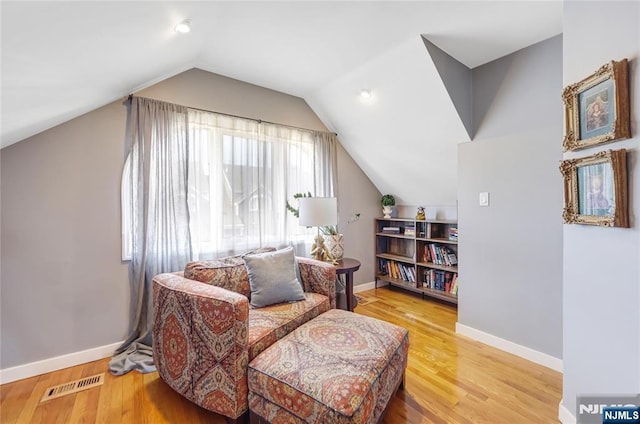 sitting room with visible vents, vaulted ceiling, baseboards, and wood finished floors