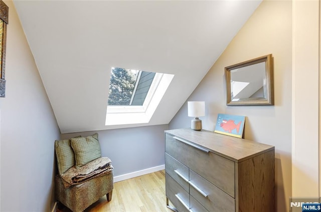 sitting room featuring light wood-type flooring, vaulted ceiling with skylight, and baseboards