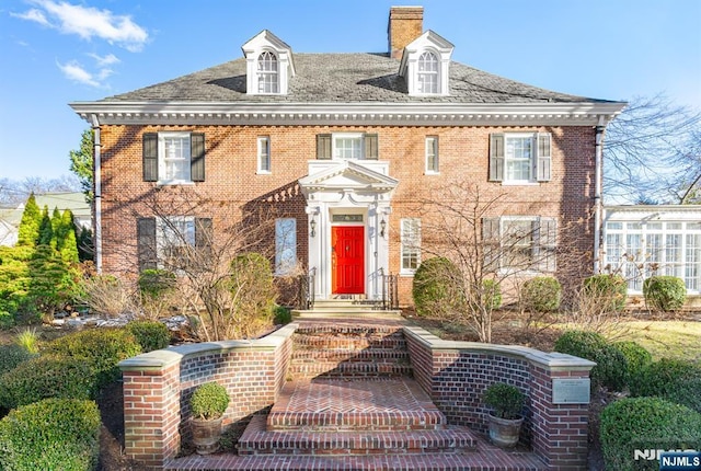 colonial inspired home featuring brick siding and a chimney