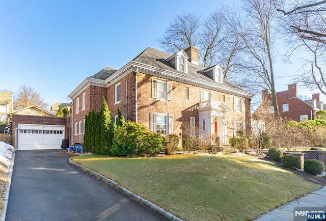 colonial home featuring brick siding, a front yard, a garage, an outbuilding, and driveway