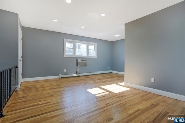 empty room with baseboard heating, light wood-type flooring, and an AC wall unit