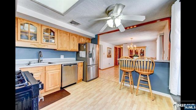 kitchen with stainless steel appliances, visible vents, light countertops, glass insert cabinets, and a sink